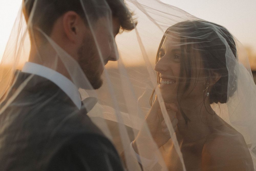 Sunlit silhouettes of a couple share an intimate moment through sheer curtains.