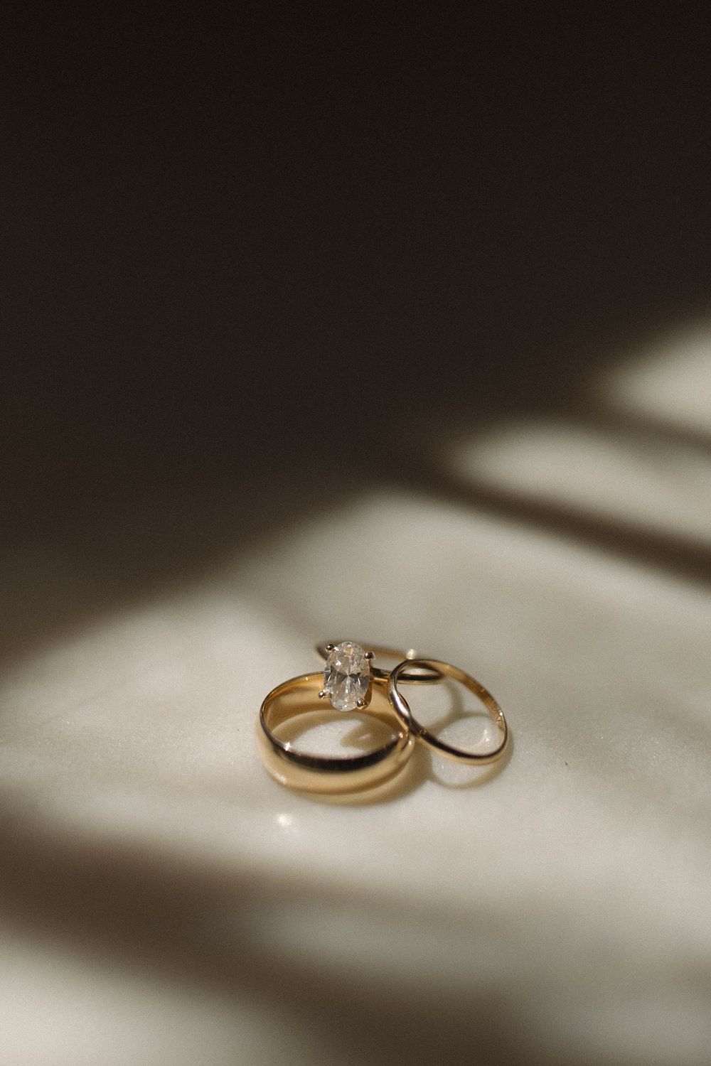 Wedding rings photographed in dramatic window light on a white surface.