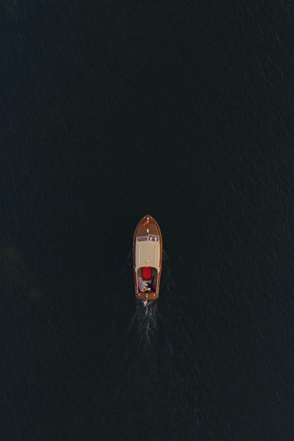 Aerial view of a wooden boat cruising through dark waters, creating a wake behind it.