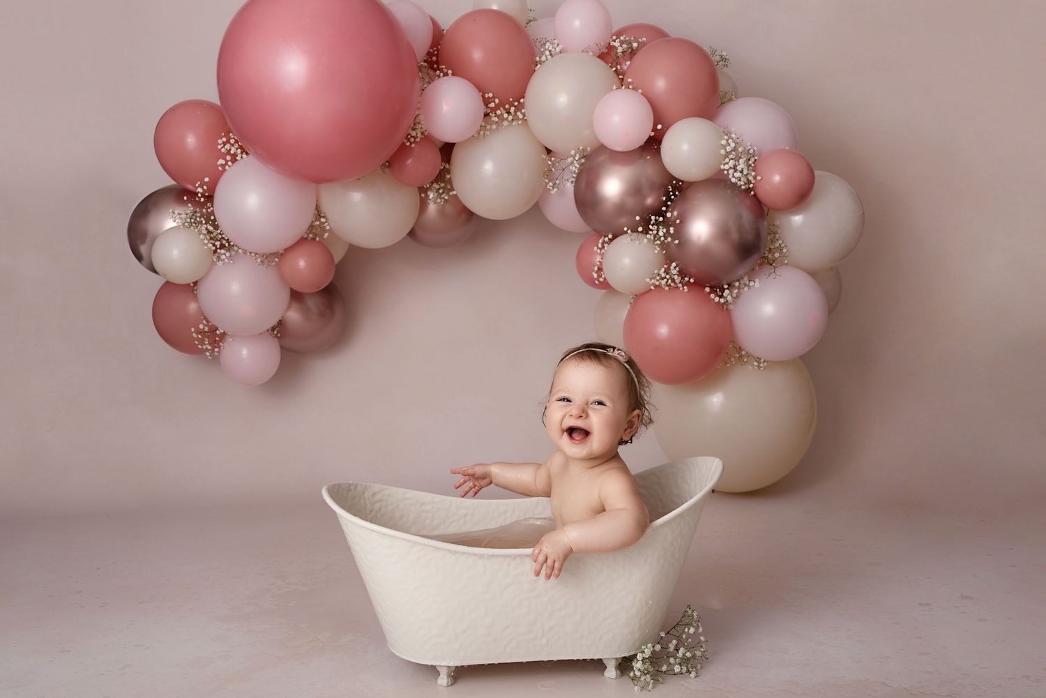 Baby Cake smash bath photoshoot with pink and white balloon arch and white tub setup.