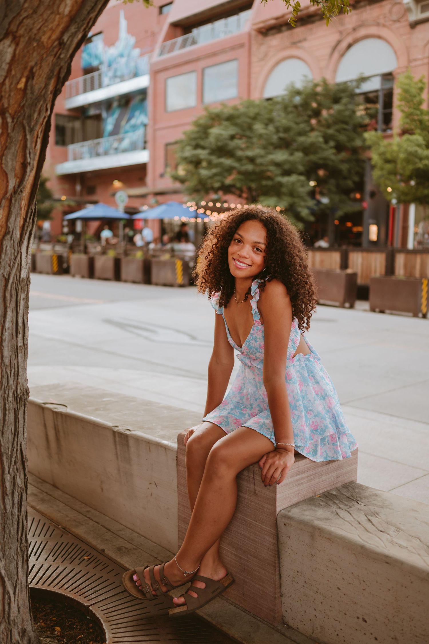 A figure in a light blue dress dances playfully on a yellow line in the middle of a city street with mountains in background.
