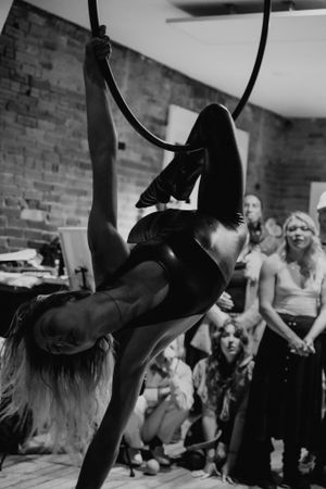 An aerial dancer executes a dynamic pose on a lyra hoop while performing for an audience.