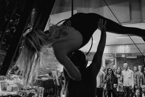 An aerial artist performs a graceful backbend while suspended on a lyra hoop in front of an audience.