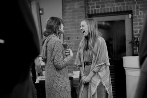 Two people in winter coats having an animated conversation against brick wall background.