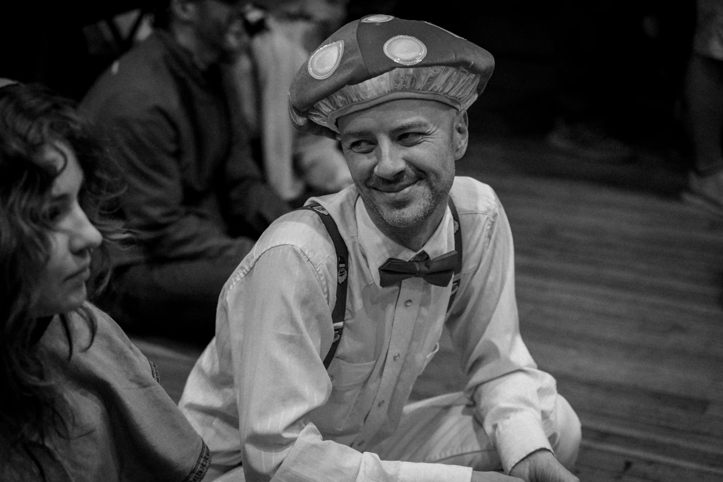 Person wearing a vintage cap and bowtie smiling in a classic black and white portrait.