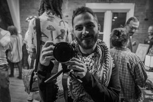 Two photographers holding cameras and smiling at an indoor event.
