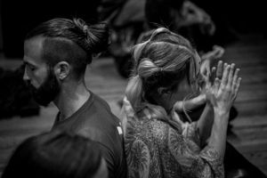 Two people in prayer or meditation pose with visible tattoos in black and white.