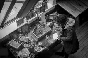 Overhead view of a person working at a cluttered desk with various items spread across the surface.