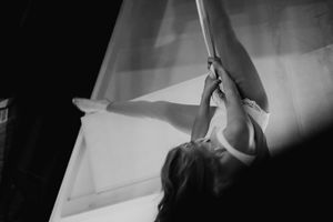A dramatic black and white shot of an aerial silk performer in mid-performance against white backdrop.