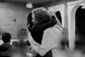 Two people embracing in an indoor venue with brick walls and arches.