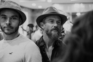 Two attendees in hats stand among a crowd at an indoor event.