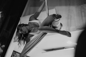 An aerial artist performs a graceful pose while suspended on silk fabrics in black and white.