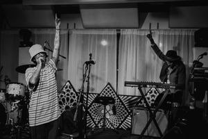 Black and white concert photo showing performers on stage with geometric patterns in the background.
