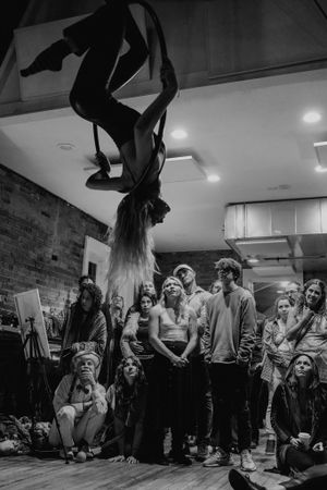 An aerial performer hangs upside down on a hoop while an audience watches in amazement.
