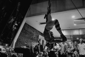 A dramatic black and white photo captures an aerial acrobat performing an inverted pose.