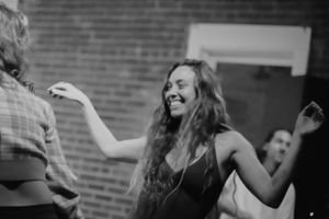 A joyful dancer moves to music in a black dress at an indoor event.