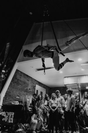 A dramatic aerial performance shot showing a suspended artist above an engaged audience.