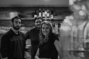 Staff members behind a bar with bottles displayed on shelves in the background.