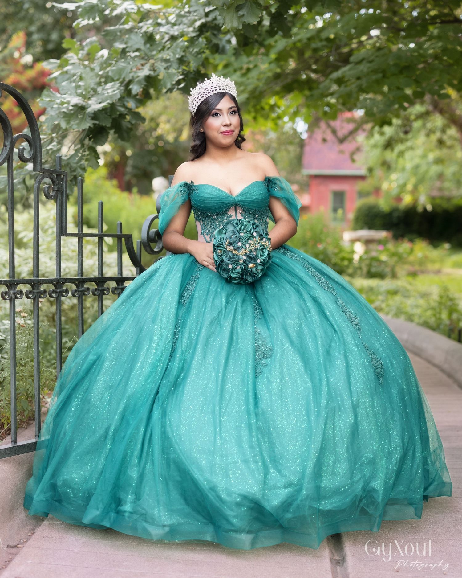 A stunning emerald green ballgown with puff sleeves and tulle skirt is showcased in an outdoor garden setting.