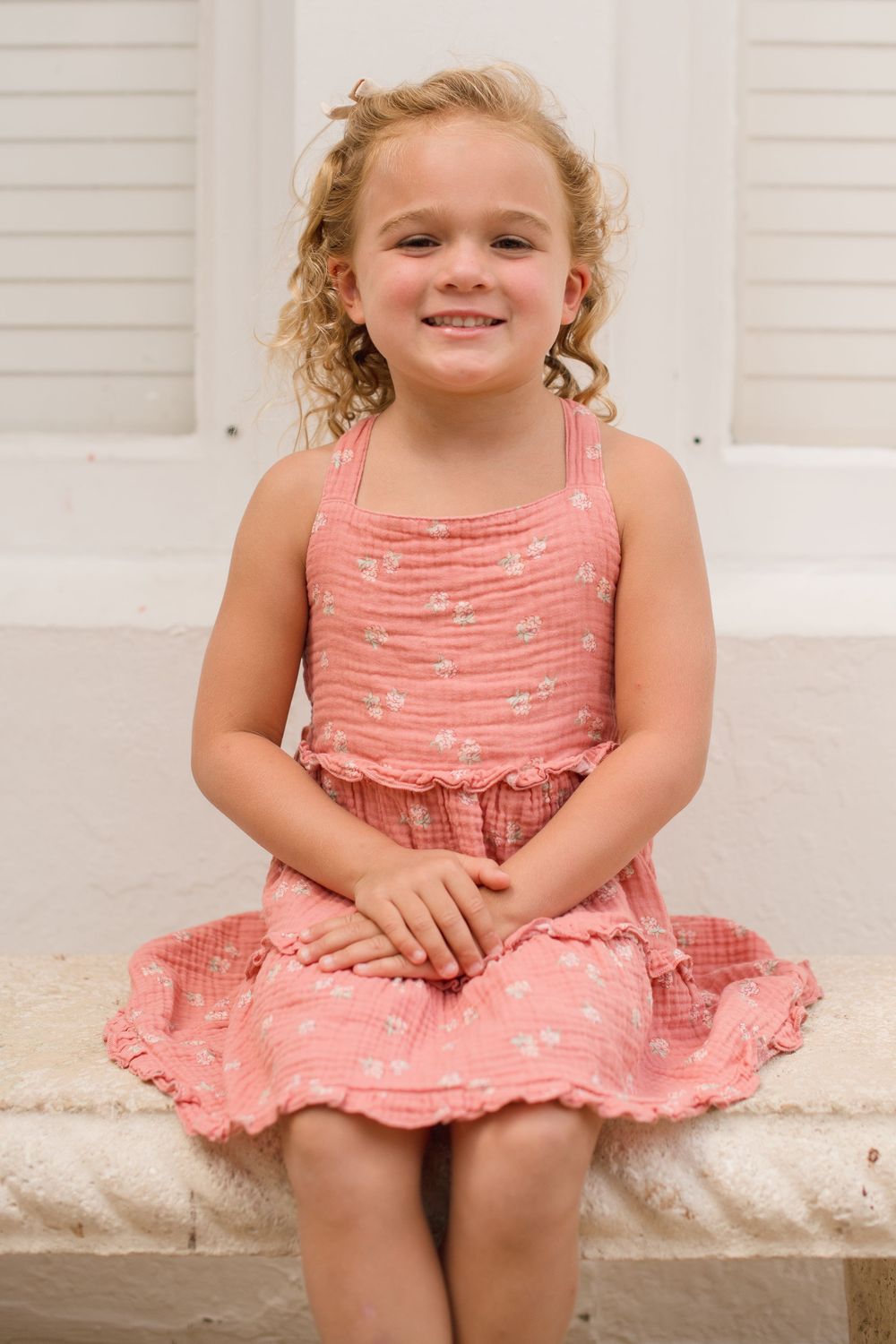 Child wearing a pink ruffled sundress sits on white steps in a collage of four similar poses.