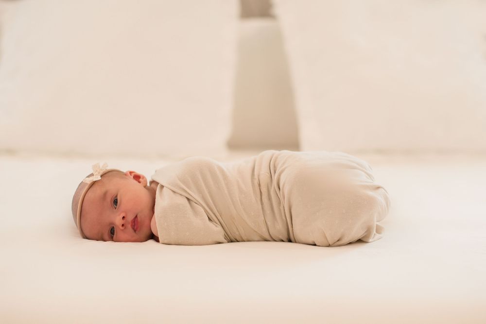 Newborn baby swaddled in cream fabric lying on white background photographed from different angles.