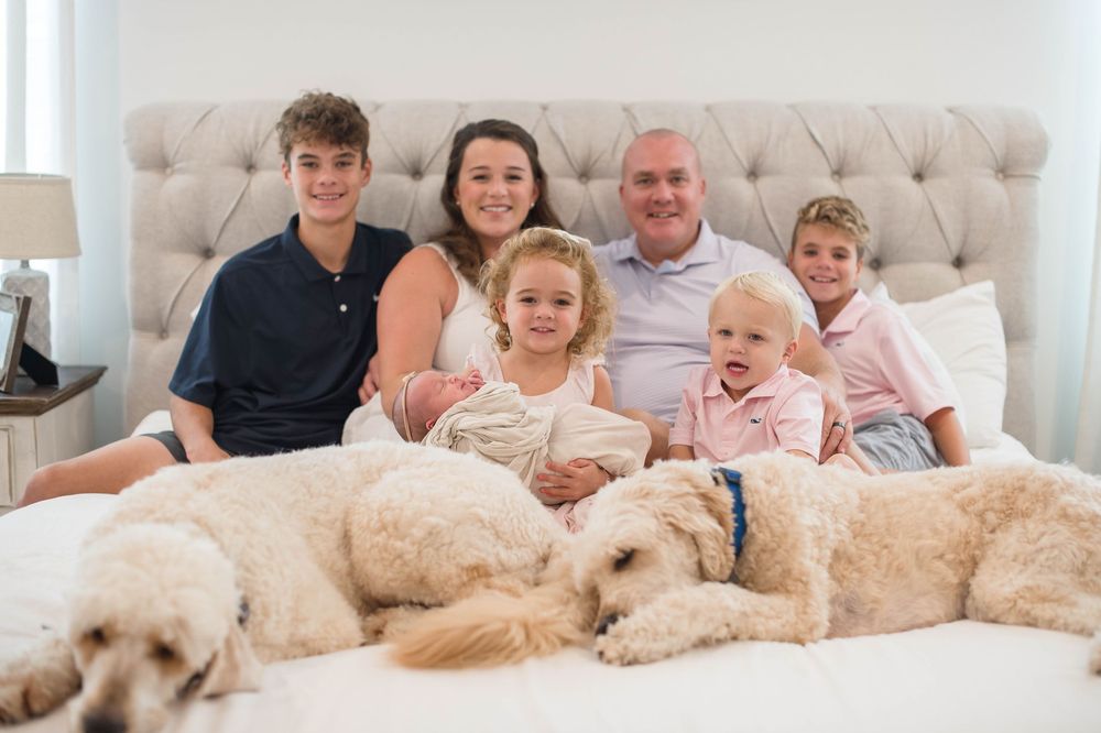 A group of people sit on a couch with multiple golden doodle dogs lounging beside them.