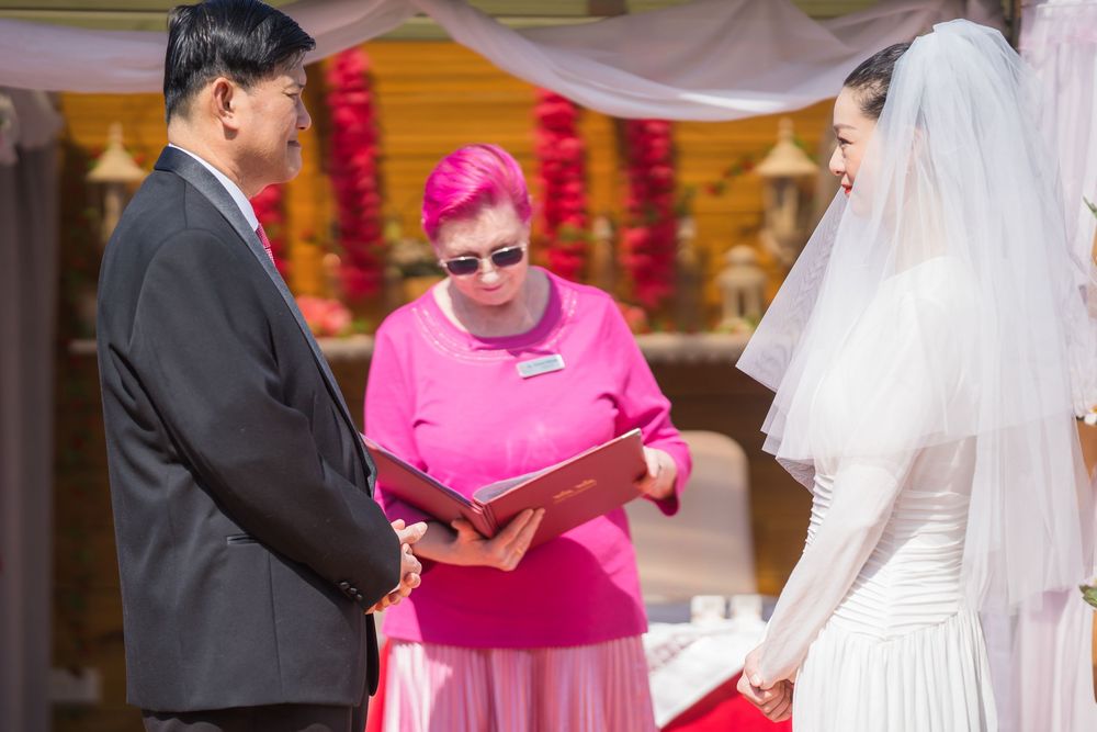 People gather at a wedding ceremony as someone in bright pink stands with others in formal attire.