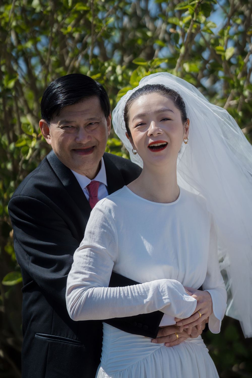 A joyful outdoor wedding scene on a sunny day with green foliage in the background.