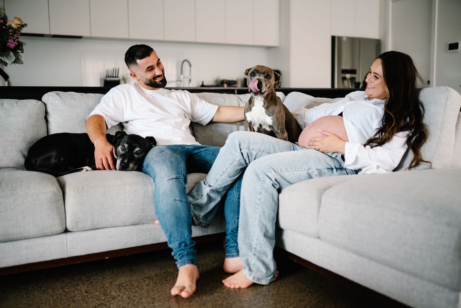 A couple relaxes on a gray sofa with their pets at home taken during an in home maternity photo session in Melbourne by Pei A Photography.