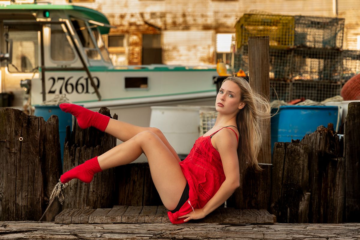 A person in a flowing red dress,  poses elegantly against a rustic wooden fence.