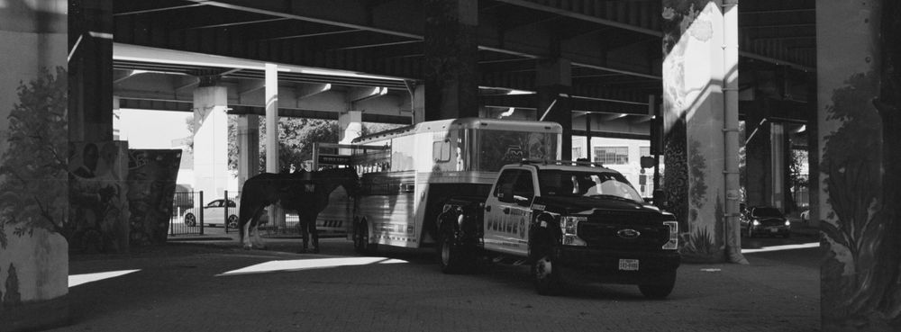 A black and white panoramic urban streetscape showing empty cityscapes, building silhouettes, and geometric shadows.