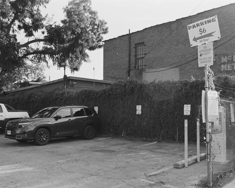 A black and white panoramic view of cars parked against a brick wall in an urban setting.
