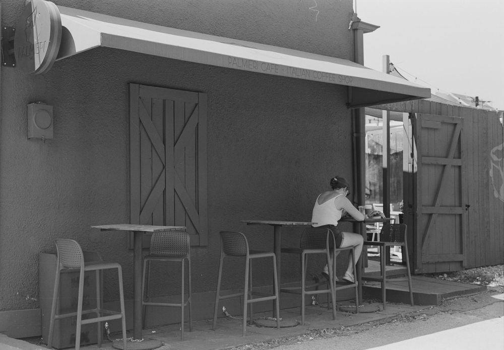 A simple outdoor cafe or snack bar with bar stools and wooden doors in a vintage black and white photograph.