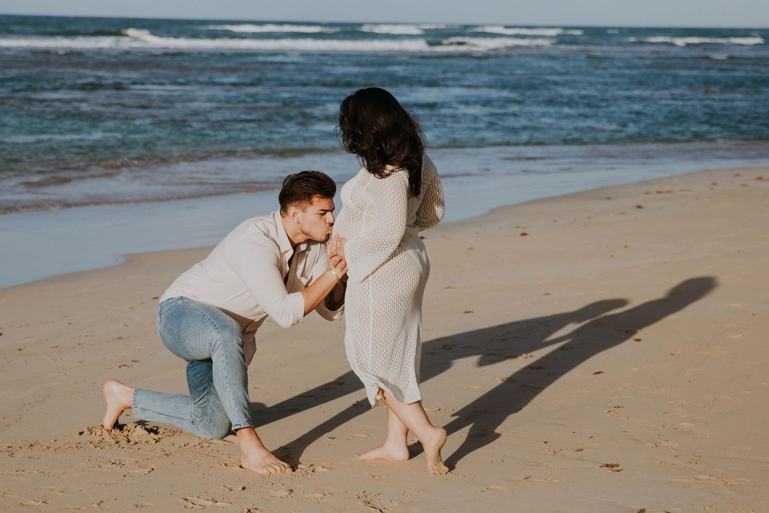 A romantic beach proposal scene at sunset with crashing waves in the background.
