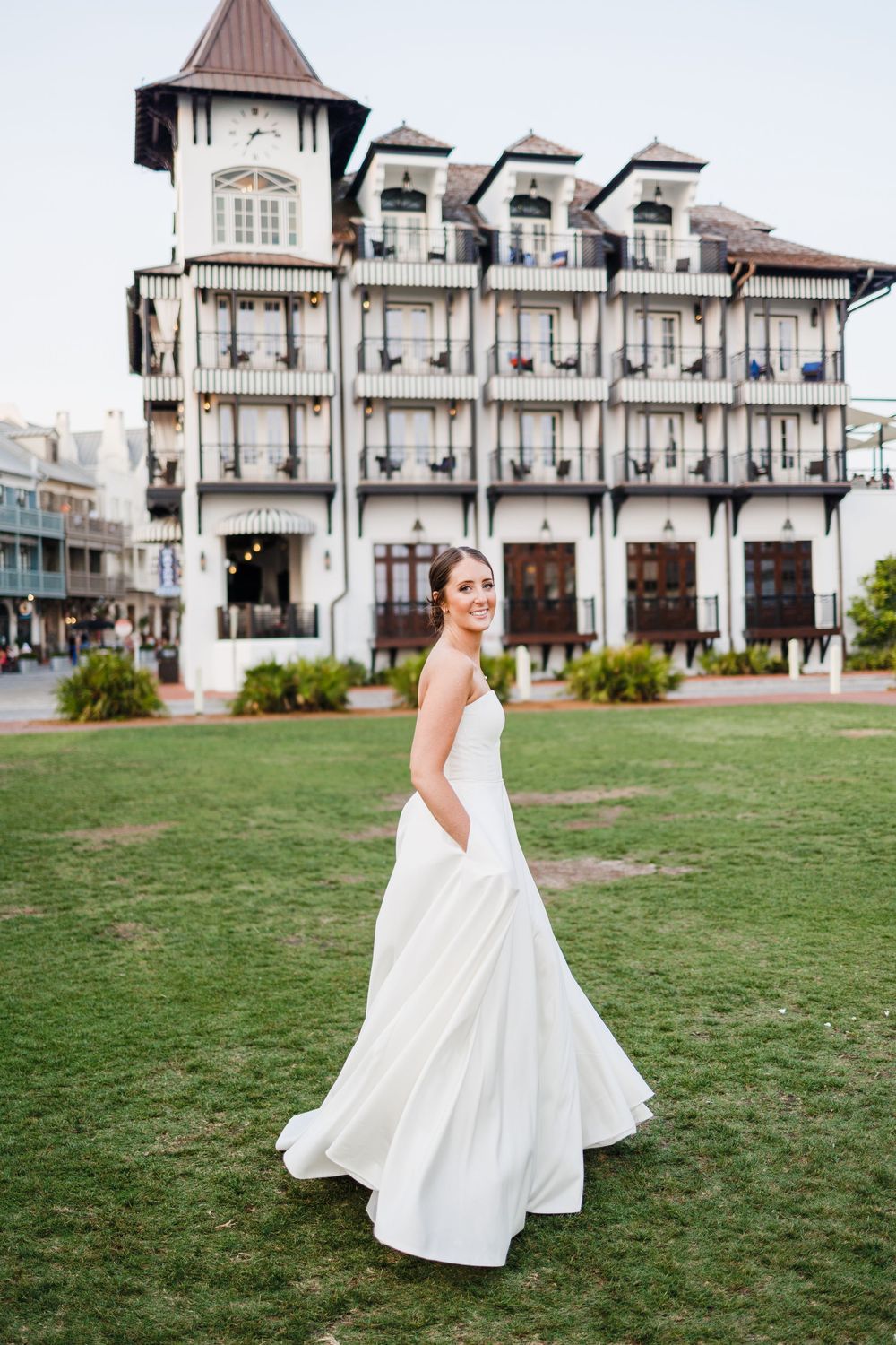 A flowing white wedding dress twirls gracefully on a green lawn in front of a grand Victorian-style mansion.