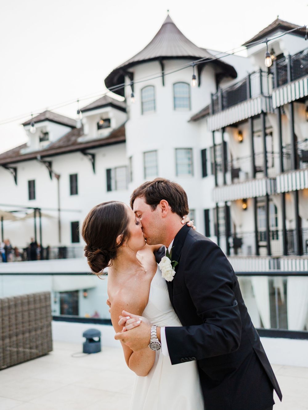 A romantic wedding moment captured at a luxury hotel venue with elegant white architecture and balconies.