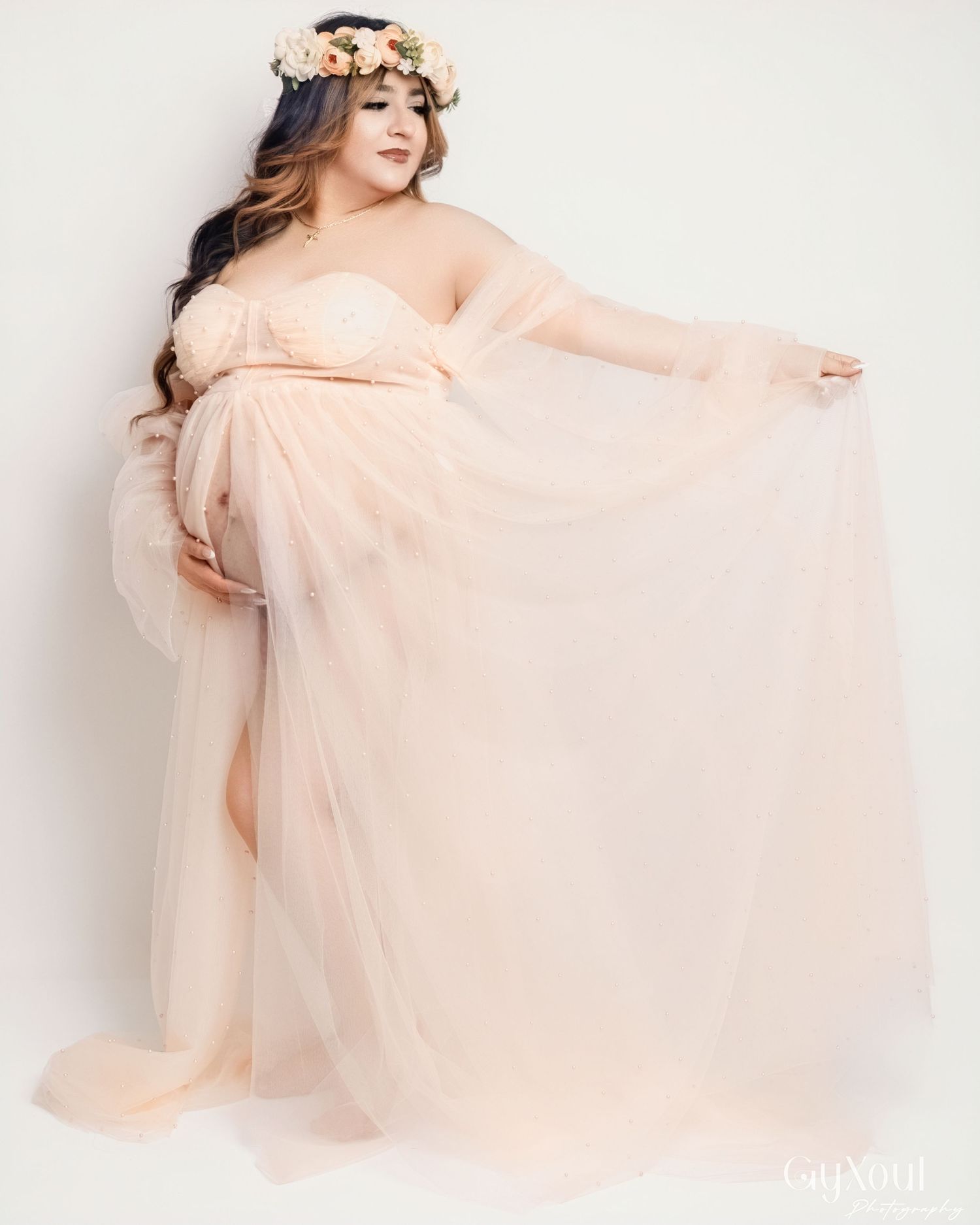 Woman in blush pink tulle dress poses gracefully against white background in romantic boudoir photoshoot.