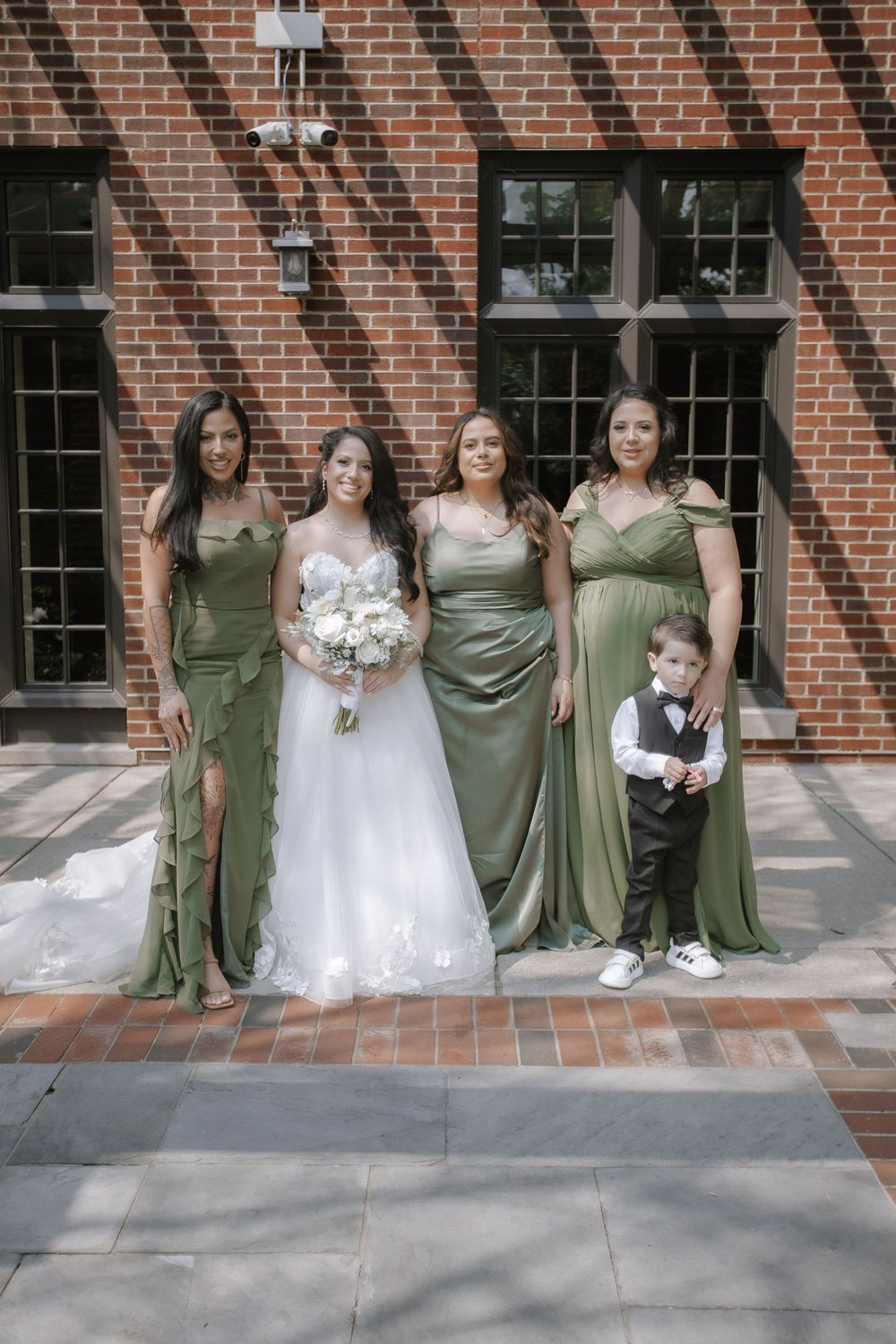 Wedding party with bridesmaids in sage green dresses posed outside brick building.