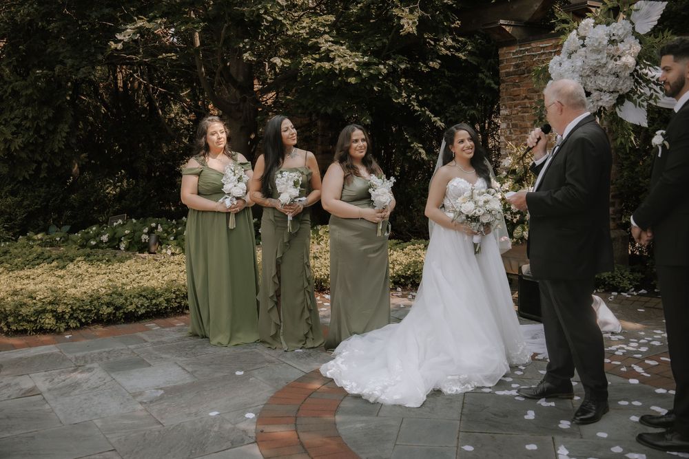 Wedding party arranged on a brick path with bridesmaids in sage green dresses.
