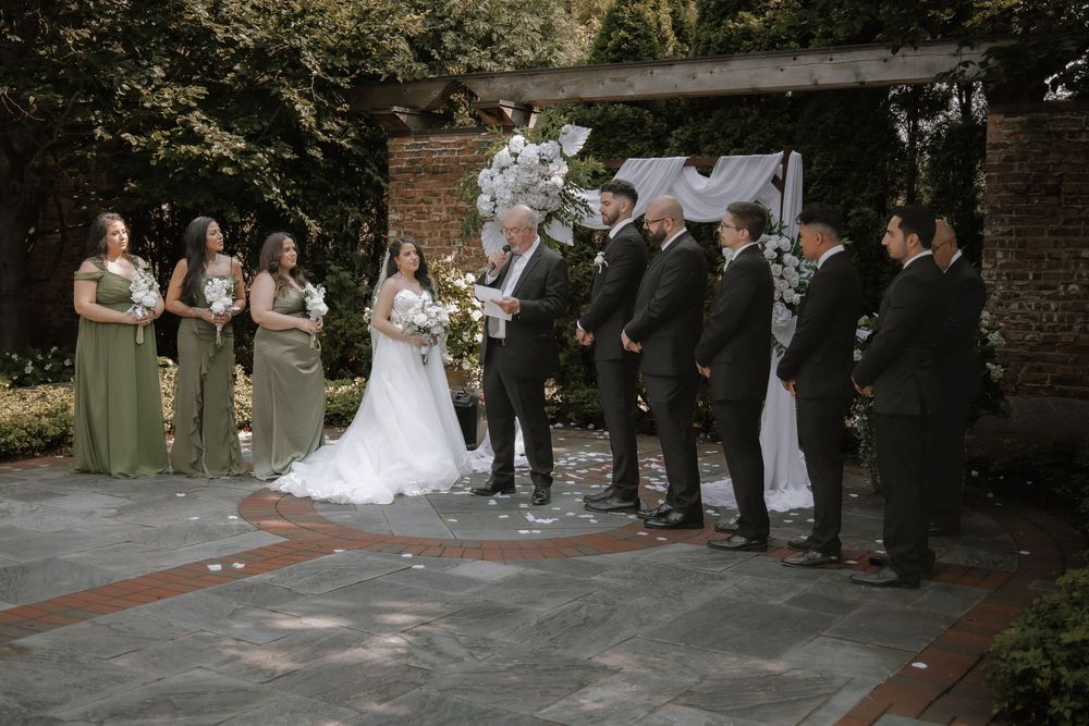 A wedding party lined up beside a rustic brick wall during an outdoor ceremony.