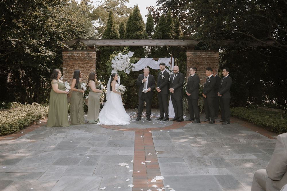 Wedding party stands in formation against a brick wall backdrop during an outdoor ceremony.