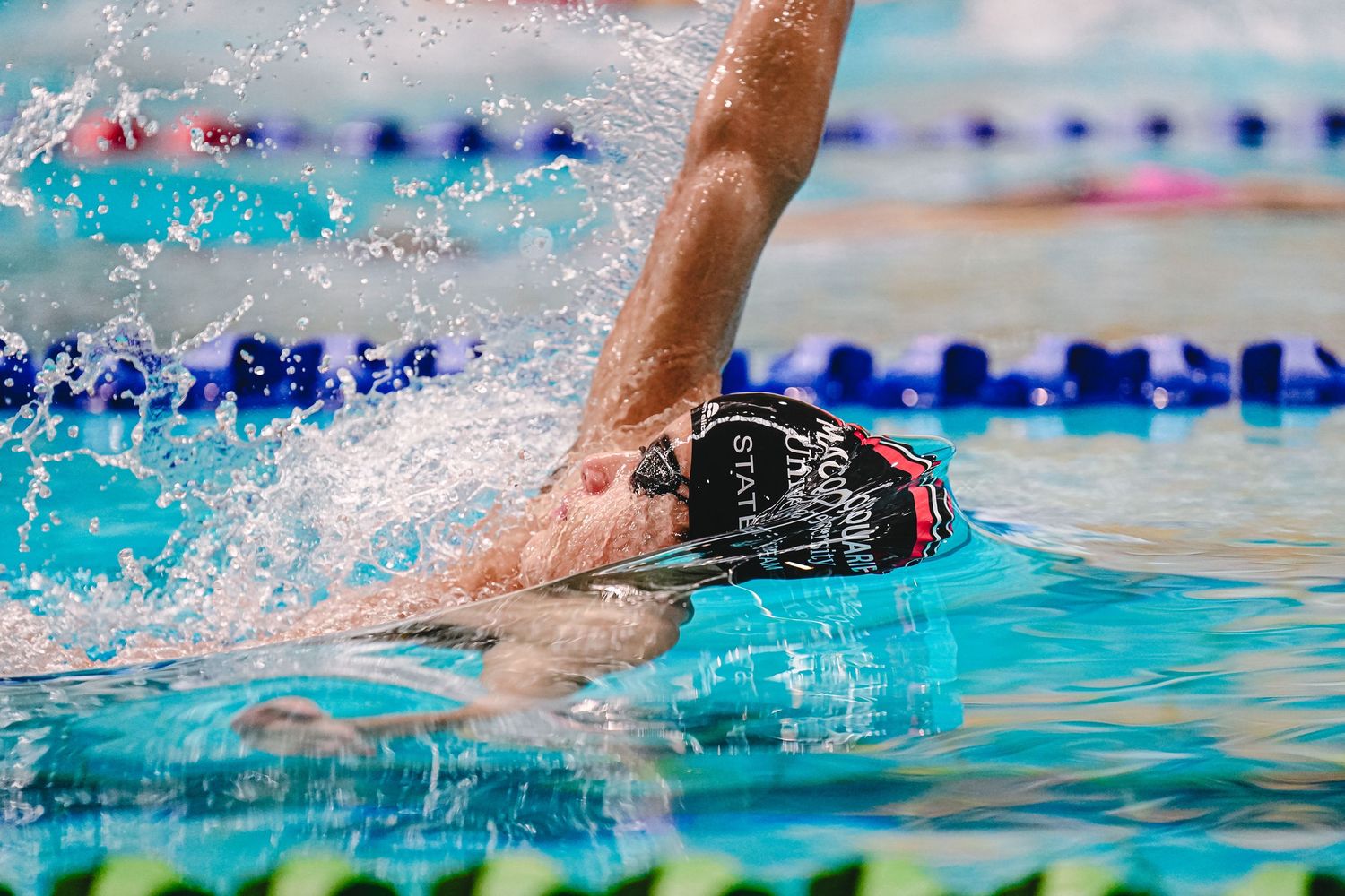 Competitive swimmer performing freestyle stroke in bright blue pool water with splashes during race competition.