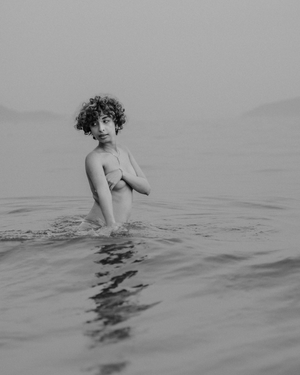 Artistic black and white portrait of a nude figure emerging from calm waters.