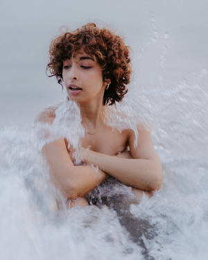 Artistic water portrait of a person with curly hair amid splashing waves.