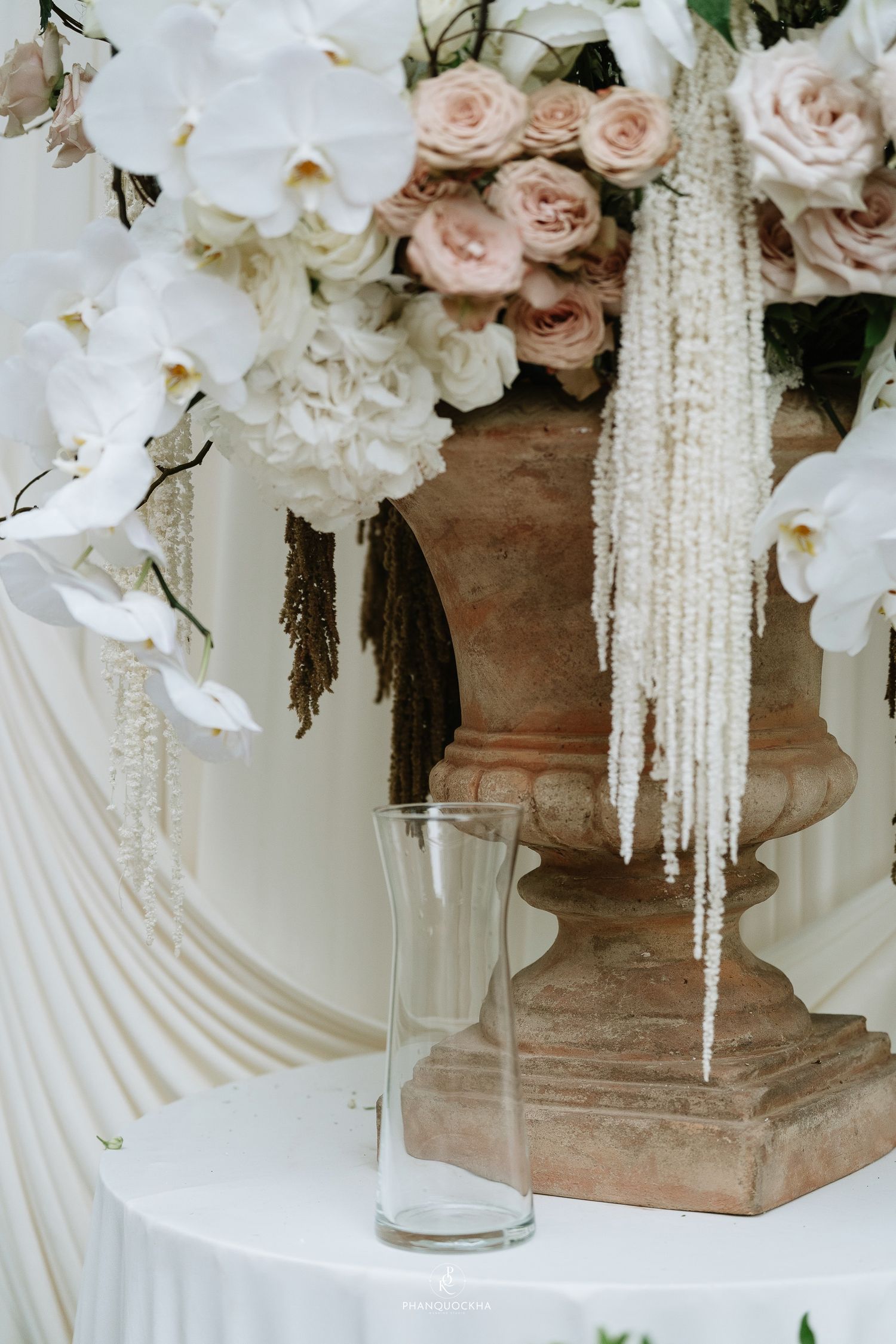 Elegant terracotta urn wedding centerpiece with white orchids, blush roses, and cascading white amaranthus.