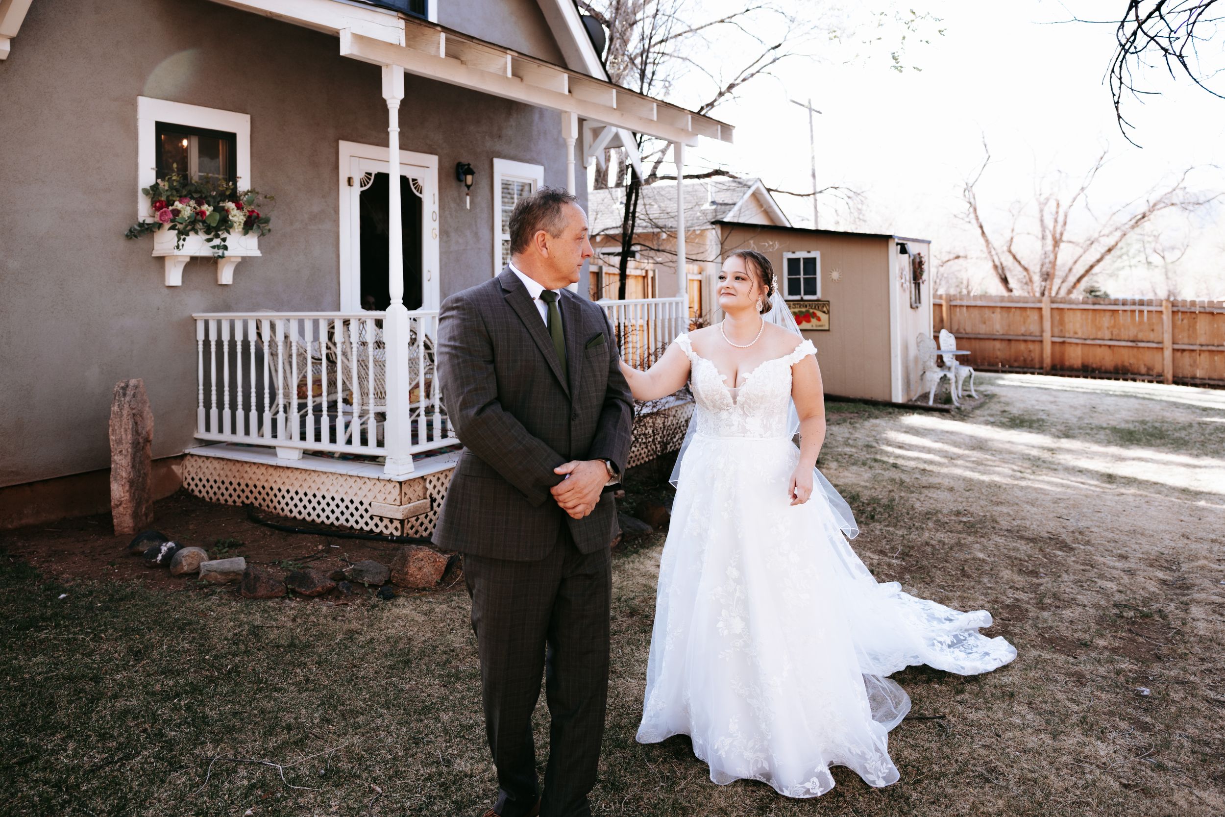 A couple shares a moment on their wedding day in front of a house with white porch railing.