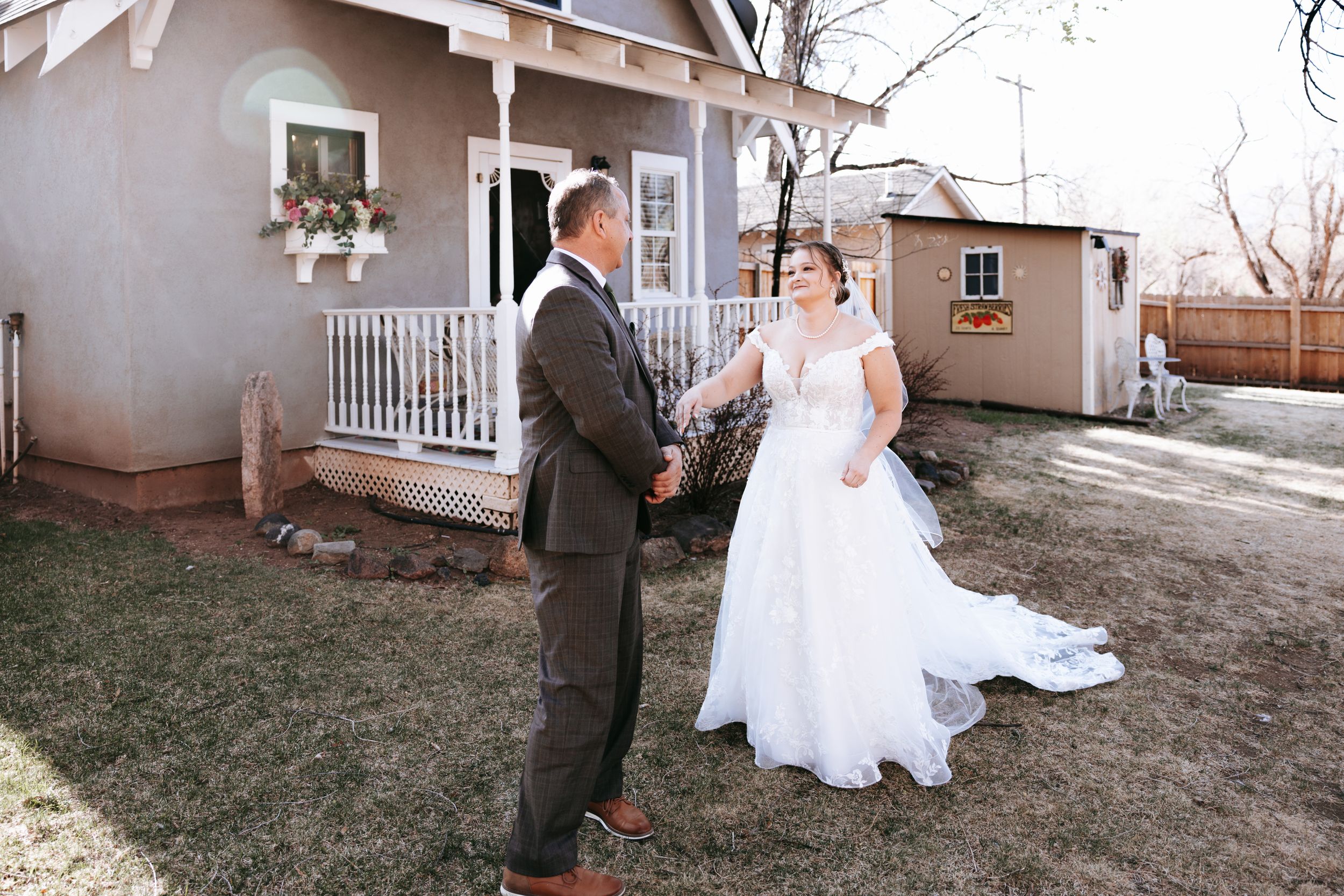 A wedding couple shares a moment in front of a charming house with a white porch railing.