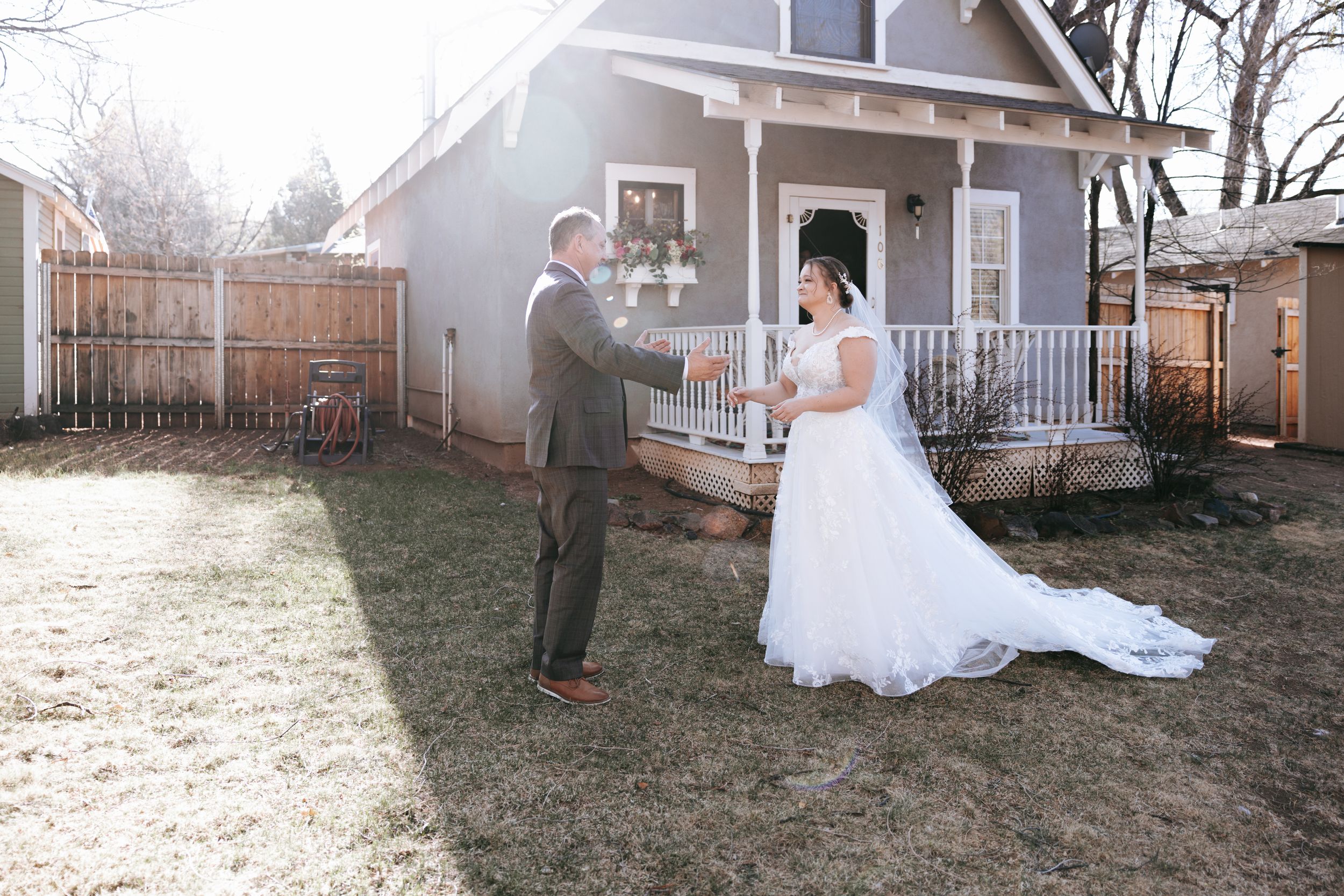 A rustic backyard wedding scene with a couple in front of a grey house with white trim.