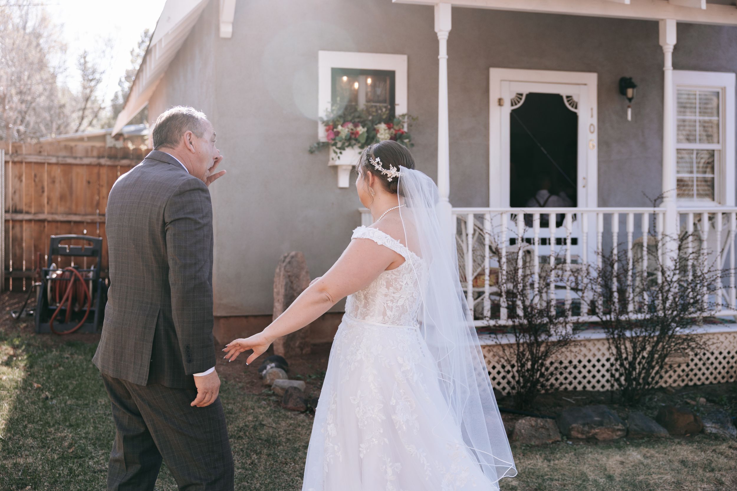 A wedding couple hold hands while walking in front of a grey craftsman style house with white porch details.