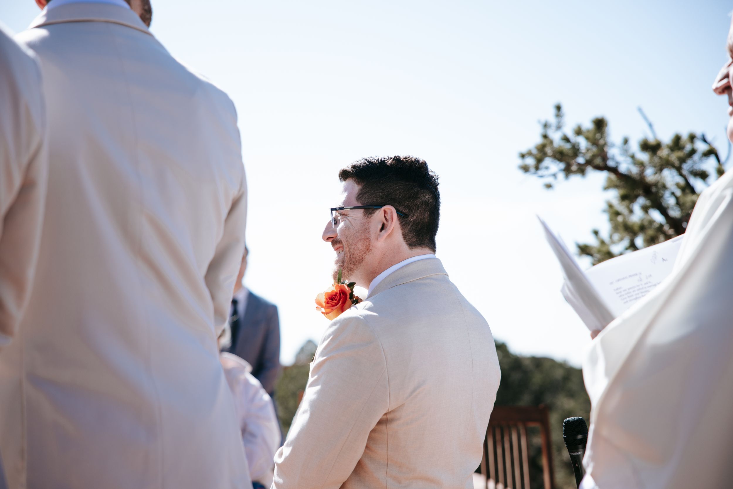 Wedding ceremony guests gathered outdoors in formal attire.